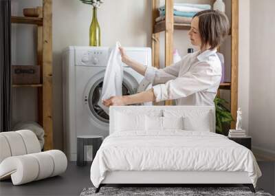 Woman is rejoiceing of white laundry washed in a washing machine in a laundry. The concept of caring for things, cleaning and hygiene Wall mural