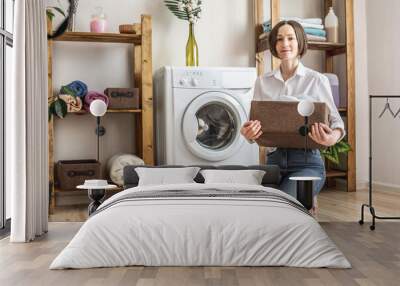 Woman is washing white clothes in a washing machine in a laundry room. The concept of caring for things, cleaning and hygiene Wall mural