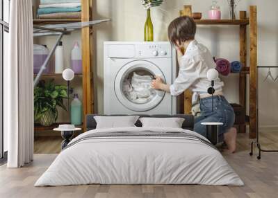 Woman is washing white clothes in a washing machine in a laundry room. The concept of caring for things, cleaning and hygiene Wall mural