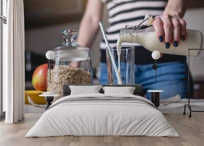 Woman pours organic oat milk from a bottle into a glass on a table in the kitchen. Diet healthy vegetarian product Wall mural