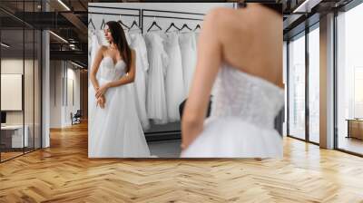 A portrait of a beautiful young bride who is trying on a white wedding dress in a store is reflected in the mirror. Wall mural