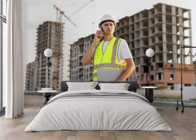 Architect is talking on the phone at a construction site in a protective helmet and vest. Wall mural