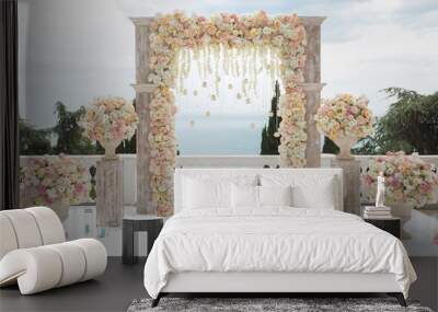 Elegant wedding arch with fresh flowers, vases on background of ocean and blue sky. Wall mural