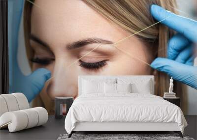 Cosmetologist plucks client eyebrows by thread Wall mural