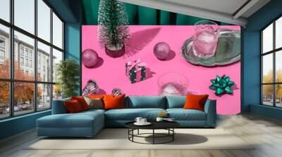 Pacific pink retro futuristic Christmas table arrangement with a tree, gift, bow, pink ice cold cocktails in crystal glass with emerald green curtain background. New Year's eve dinner party aesthetic. Wall mural