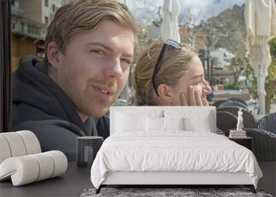 Young handsome couple sit in cafe and squint in stark sunshine Wall mural