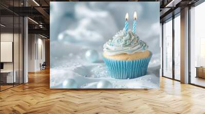 A frosted cupcake with two lit candles on a blue background. Wall mural