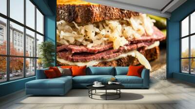 A close-up of a classic Reuben sandwich with corned beef, Swiss cheese, sauerkraut, and Thousand Island dressing on rye bread, served with a side of pickles Wall mural