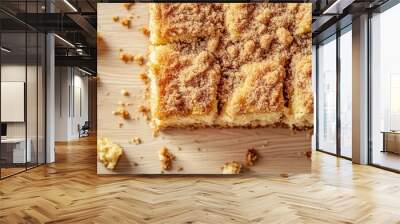 Close-up of a moist coffee cake with a crumbly streusel topping, arranged on a light wooden surface with a few crumbs. Wall mural