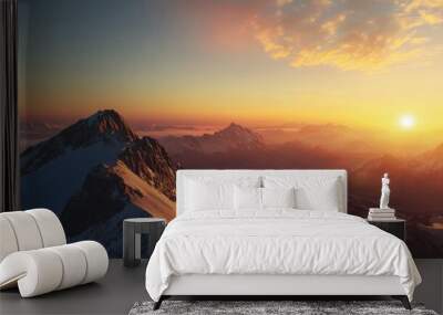 Flat lay of a mountain summit at sunset, with the sun casting a warm glow over the peaks and the valley below covered in shadow. Wall mural