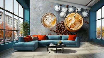 Flat lay of an iced latte and a glass of cold water with ice cubes, surrounded by coffee beans and a straw on a textured grey surface. Wall mural