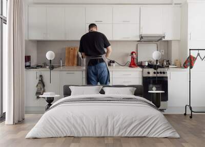 Back view of a man busy cooking in a well-equipped, bright kitchen. Wall mural