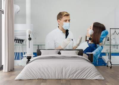 Caucasian male dentist examining young woman patient's teeth at dental clinic. Doctor probing teeth with dental instrument using an explorer look for cavities treatment and checking problems Wall mural