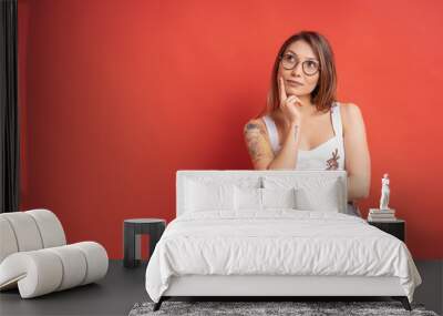 Caucasian woman with glasses thinking and imagination isolated on red background Wall mural