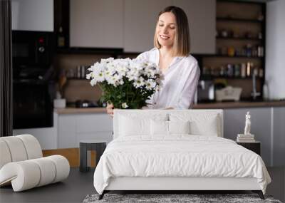 Happy and joyful young woman in white arranging white flowers at home in the kitchen Wall mural