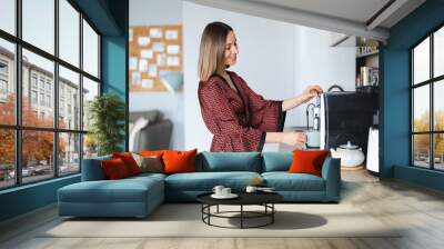 Woman using coffee machine to make big mug of coffee at home. Woman wearing silk robe at home while preparing a latte Wall mural