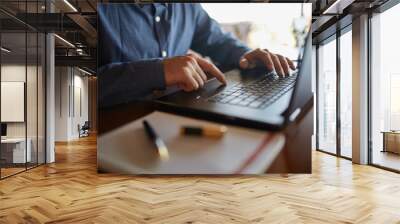 Close-up photo of caucasian male hands typing on laptop keyboard and using touchpad. Notebook and pen on foreground of workspace. Business man working on computer. Isolated no face view. Wall mural