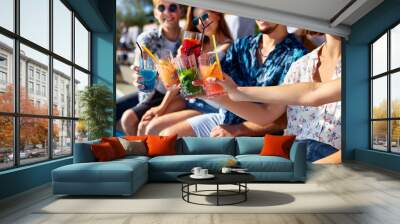 Close view. Friends clinking glasses with fresh colorful cocktails sitting by swimming pool on sunny summer day. People toast drinking beverages at luxury villa poolside party on tropical vacation. Wall mural