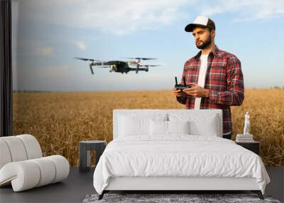 Compact drone hovers in front of farmer with remote controller in his hands. Quadcopter flies near pilot. Agronomist taking aerial photos and videos in a wheat field Wall mural