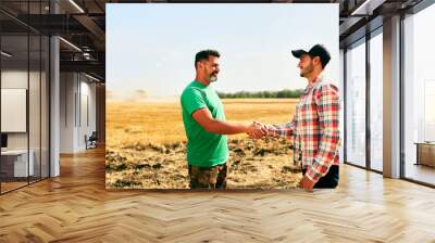 Farmer and agronomist shaking hands in wheat field after agreement. Agriculture business contract concept. Corporate farmer and landlord rancher negotiate with handshake. Combine harvesters harvest. Wall mural