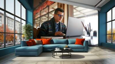 Handsome freelancer businessman working on laptop in cafe. Blogger man updating his profile in social networks with photos sharing with followers multimedia using notebook with wifi. Nerd in glasses. Wall mural