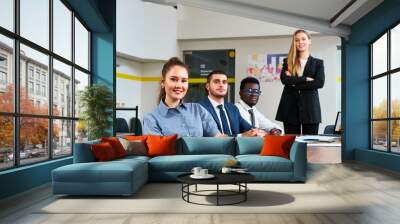 Smiling multiethnic team in office setting. Caucasian woman leads discussion with team. African, Asian colleagues engage with confidence. Professional, smart attire, collaborative work space. Wall mural