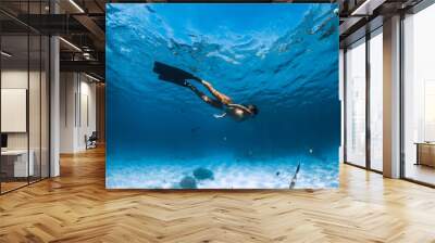 Freediver girl with fins glides over sandy bottom with fishes in blue ocean Wall mural