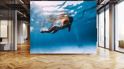 Freediver girl with fins glides over sandy bottom with fishes in blue ocean Wall mural