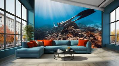 Woman freediver with diving fins glides on coral reef. Freediving in blue ocean with sun rays Wall mural