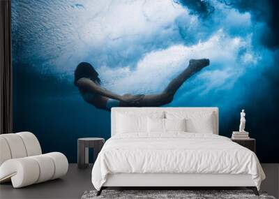 Woman under breaking wave with foam in blue ocean. Duck dive under crashing waves Wall mural