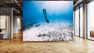 Young woman free diver glides over sandy sea with fins. Freediving in blue ocean Wall mural