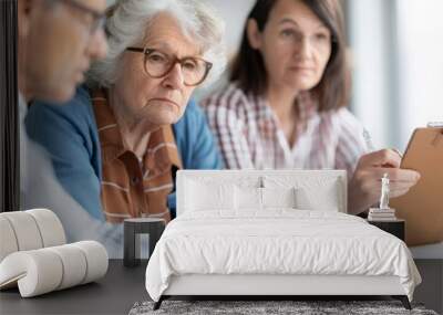 A family gathered around a table discussing financial issues while an elderly person looks on suggesting the burden of financial support on families with impoverished seniors Wall mural