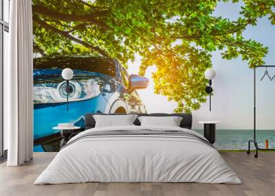 Blue sport SUV car parked by the tropical sea under umbrella tree. Summer vacation at the beach. Summer travel by car. Road trip. Automotive industry. Hybrid and electric car concept. Summer vibes. Wall mural