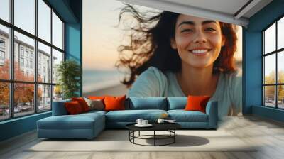 Close-up of a Hispanic woman riding a bicycle along a coastal road, her hair flowing in the wind, with the ocean in background. Freedom, joy, and beauty of outdoor adventure on a sunny day by the sea. Wall mural