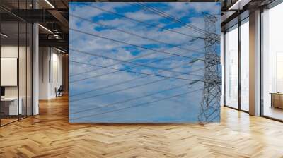 High voltage electric pylon and electrical wire against blue sky and clouds. Bottom view of electric pylon. High voltage grid tower with wire cable. Transmission lines on high voltage grid tower. Wall mural