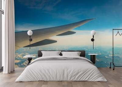 Wing of plane over mountain cover with white snow. Airplane flying on blue sky. Scenic view from airplane window. Commercial airline flight. Plane wing. Flight mechanics concept. International flight. Wall mural