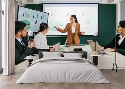 A cheerful and confident Asian businesswoman stands, present bar charts data from projector screen to her office colleagues. Asian business women leader role at the meeting. Wall mural