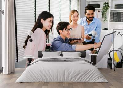 Cheerful young group of Asian businessmen in casual with one sitting and pointing at the computer display and colleagues discussing around him during the meeting. Diversity of businessmen in a meeting Wall mural