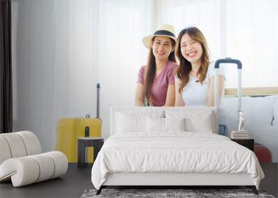 Two happy Asian women looking at the camera while sitting together on the bed with their luggage. Planning on a holiday vacation trip. Image with copy space. Wall mural