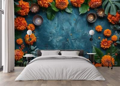 Burning diya lamps with orange flowers and green leaves border arrangement on blue textured surface, сopy space in center, flat lay. Indian festival aesthetics. Diwali celebration with nature elements Wall mural