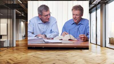 Two mature businessmen or partners readin in a book sitting at a desk with folder and book Wall mural