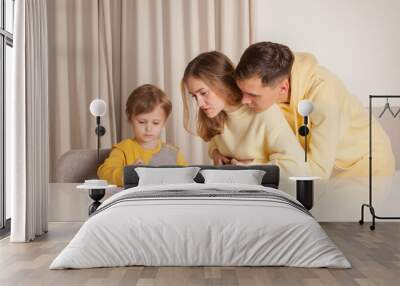 Mom and dad in yellow clothes with their child son sitting by the table and drawing Wall mural