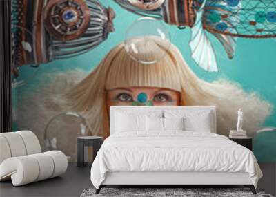 Young woman with a blonde bob hairstyle, wearing an oxygen mask with blue ornaments, leaning against the window of a spherical porthole to observe sculptures of fishes made of recycled metal objects  Wall mural