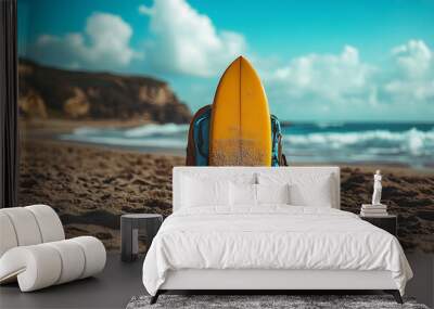 A yellow surfboard and a blue backpack on a sandy beach. Wall mural