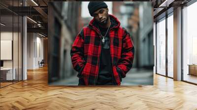 Portrait of a young man in a red and black plaid jacket standing on a city street. Wall mural