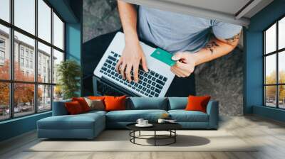 Horizontal photo of a young man paying with his credit card on a laptop. Concept of consumption and technology. Wall mural