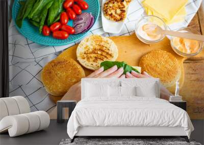 Preparation of all the ingredients for making a burger - bun, cutlet, cheese, salad, tomato, sauces. The girl s hands take a burger roll and lay the salad on top of the cutlet. Wall mural