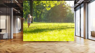 Two energetic kids, boy and girl, sprint across a lush green park bathed in warm sunlight, embodying the freedom and joy of outdoor play Wall mural