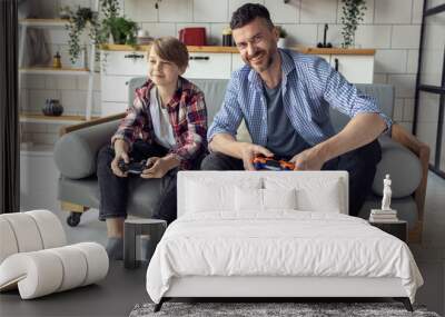 Handsome father and his teenager son spending quality time together, playing video games, sitting on the sofa at home. Having fun Wall mural