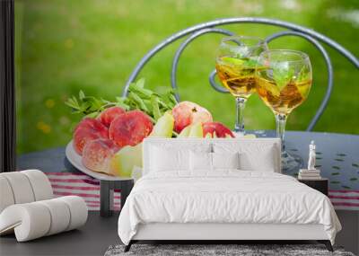 Summer party outdoor. Romantic picnic for a couple. Two glasses of cool wine served with mint and lime. Fresh melon and peach as simple light meal. Tasty low calories dessert. Green background. Wall mural